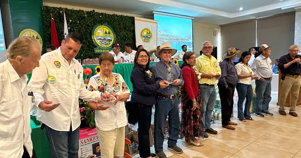Grupo de asociados y directivos de la cooperativa COOLECHE R.L. recibiendo reconocimientos de cristal durante una asamblea en un salón de eventos.